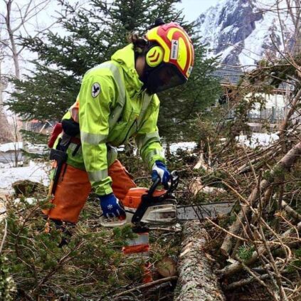hombre cortando una rama con motosierra en un pueblo que se encuentra en una montaña nevada