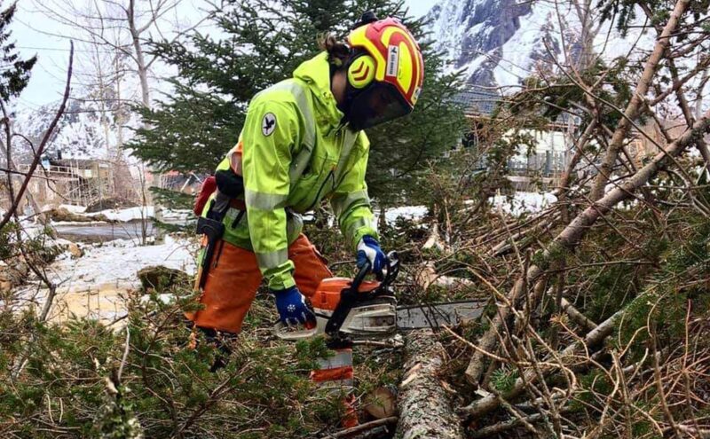 hombre cortando una rama con motosierra en un pueblo que se encuentra en una montaña nevada